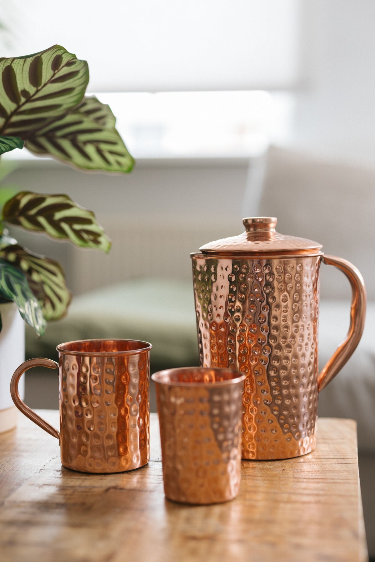 Kopero Jarro de cobre Martelado, com uma caneca e um copo sobre uma mesa de madeira