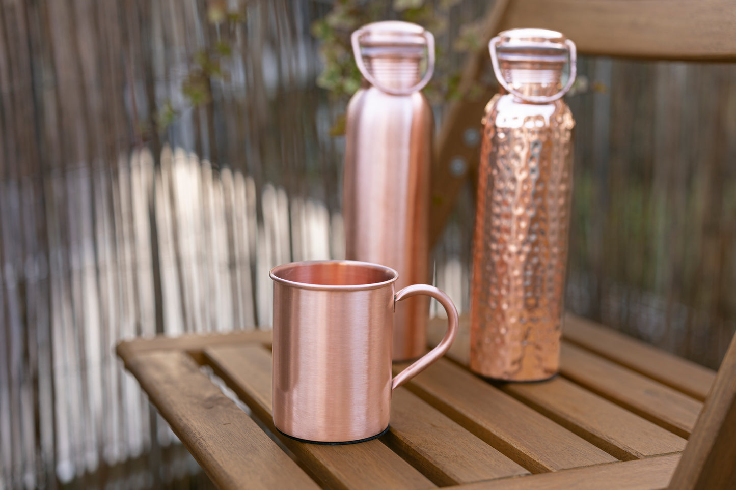 Garrafas de água de cobre Kopero Lisa e Martelada com uma caneca de cobre a condizer sobre uma mesa de jardim