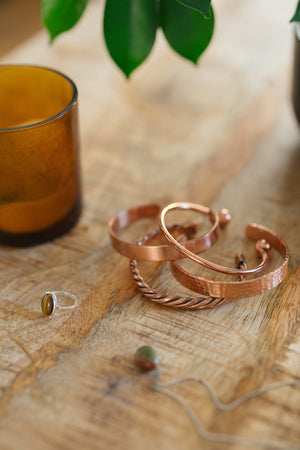 Kopero Pulseira de cobre, as quatro versões juntas sobre uma mesa de madeira com uma vela e um anel