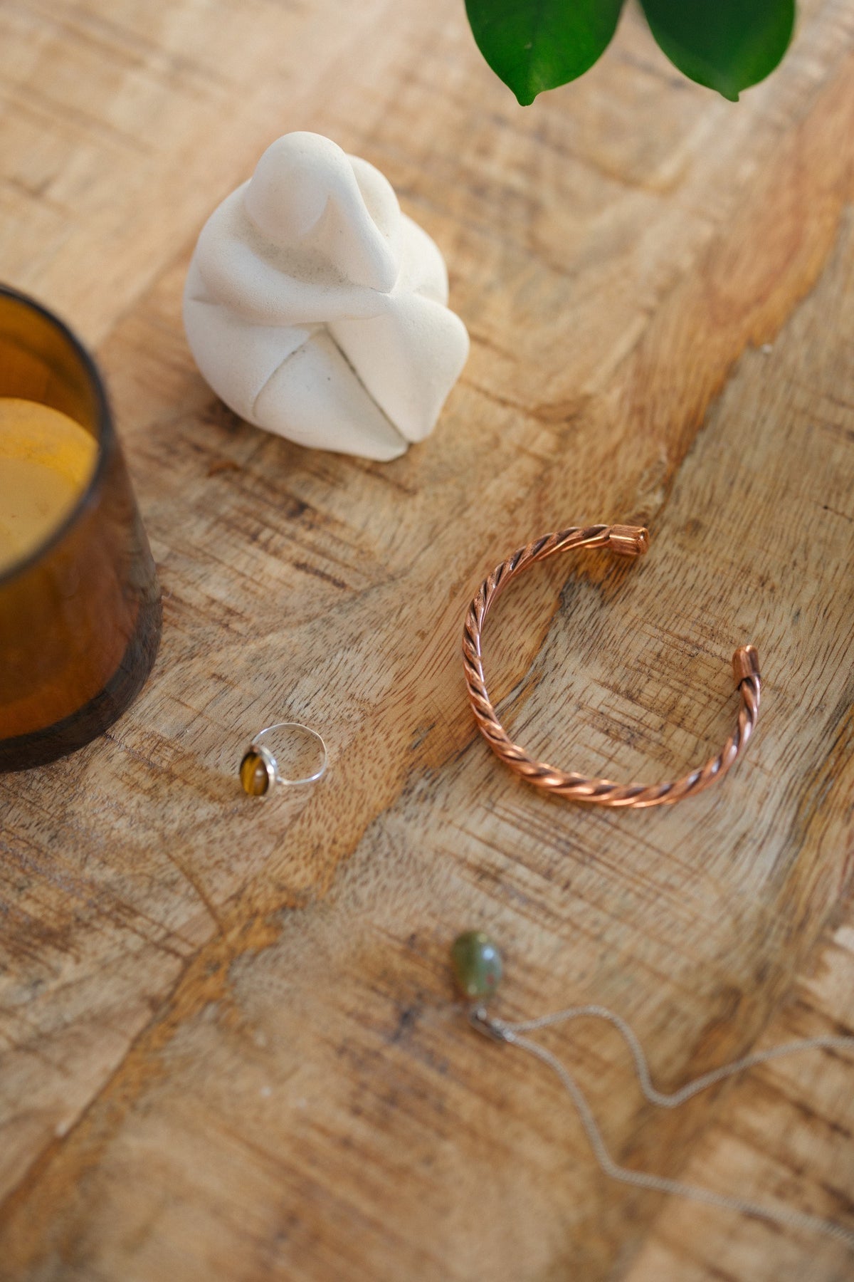 Kopero Pulseira de cobre Trançado, sobre uma mesa de madeira ao lado de uma figura e de um anel