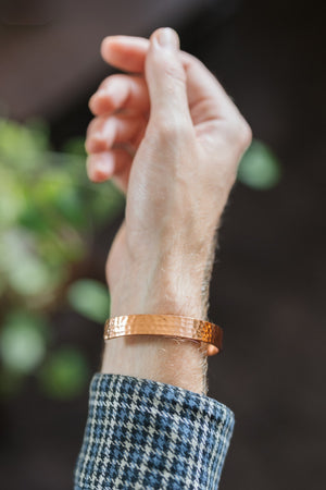 Kopero Pulseira de cobre Martelado, no pulso, com a mão levantada contra um fundo escuro