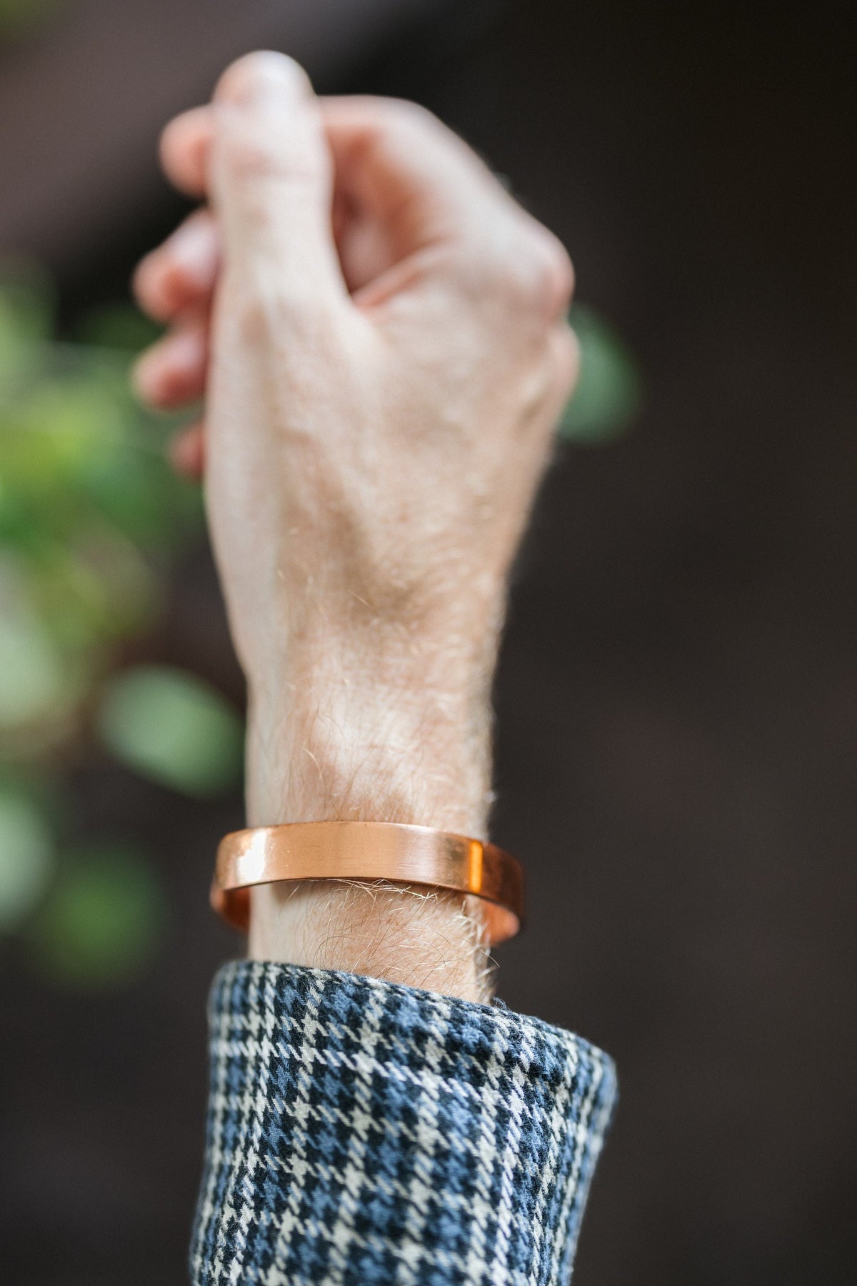 Kopero Pulseira de cobre Liso, no pulso, com a mão levantada contra um fundo escuro