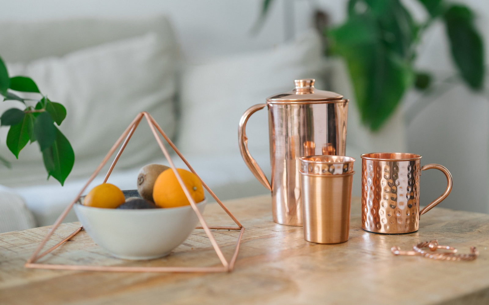 Pirâmide de cobre sobre uma taça de fruta, com um jarro, um copo, uma caneca e uma pulseira numa mesa de madeira