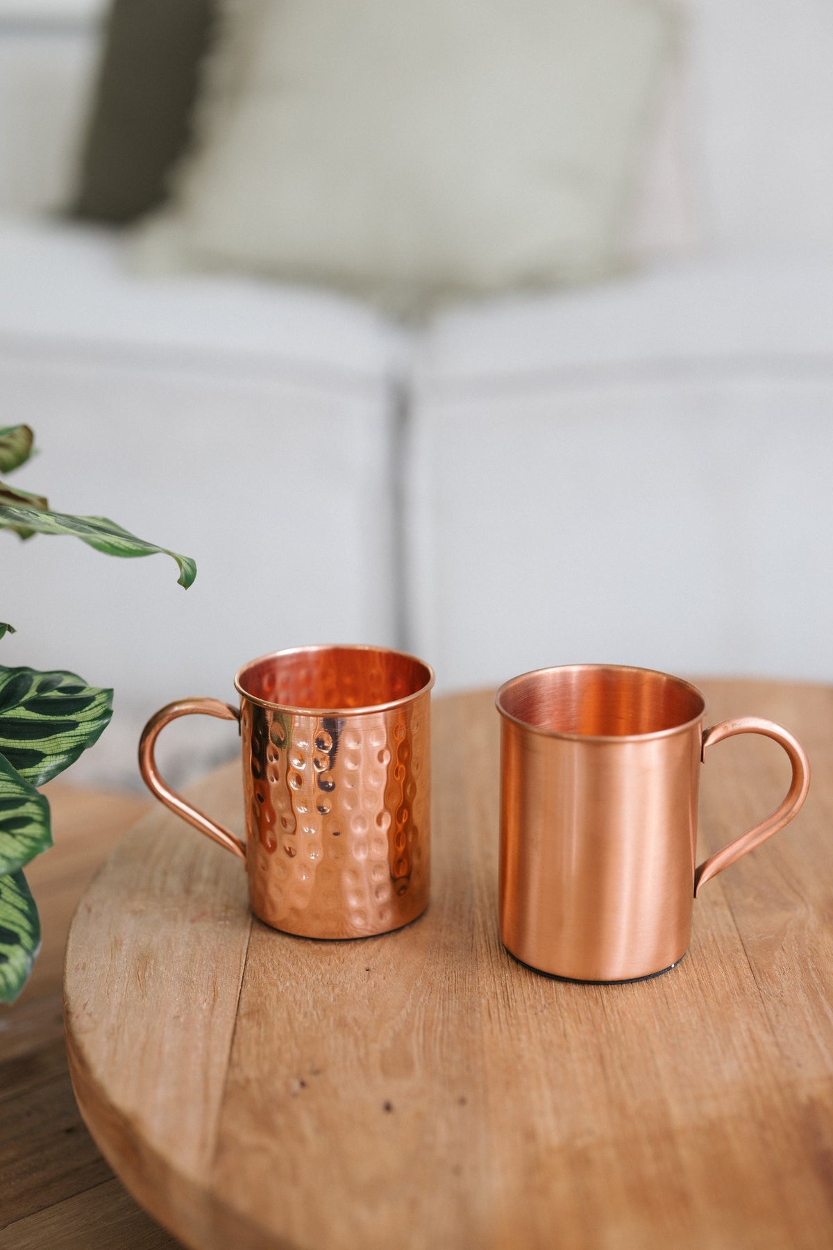 Kopero Caneca de cobre, uma caneca lisa e uma martelada lado a lado sobre uma mesa redonda de madeira