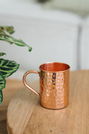 Kopero Caneca de cobre Martelado, sobre uma mesa redonda de madeira em frente a um sofá