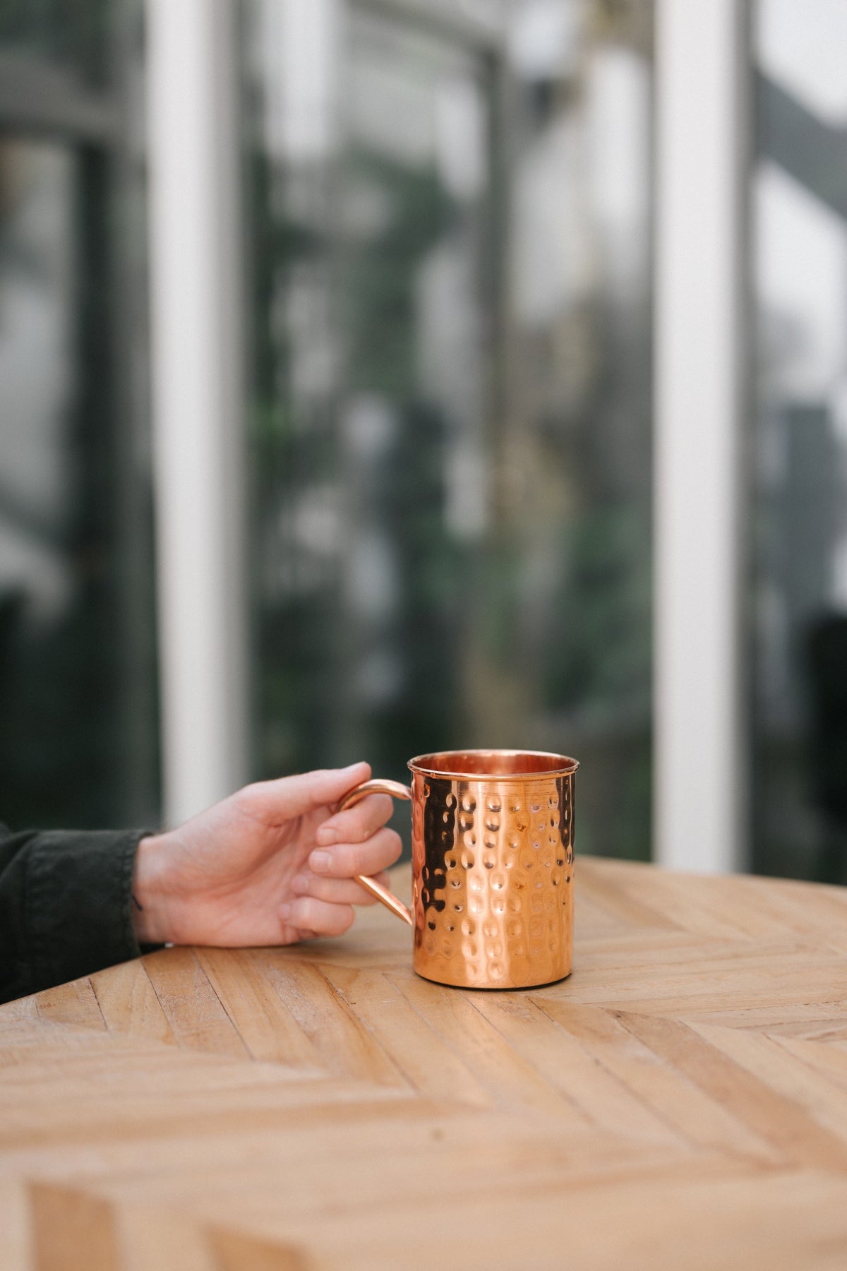 Kopero Caneca de cobre Martelado, numa mesa de madeira, com uma mão na pega