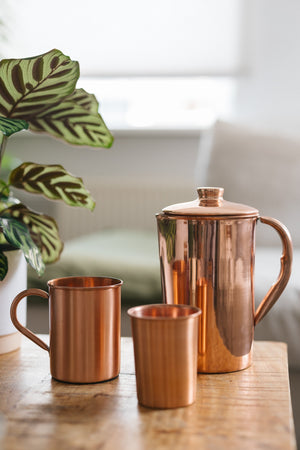 Kopero Caneca de cobre Liso, ao lado de um copo e de um jarro do mesmo cobre