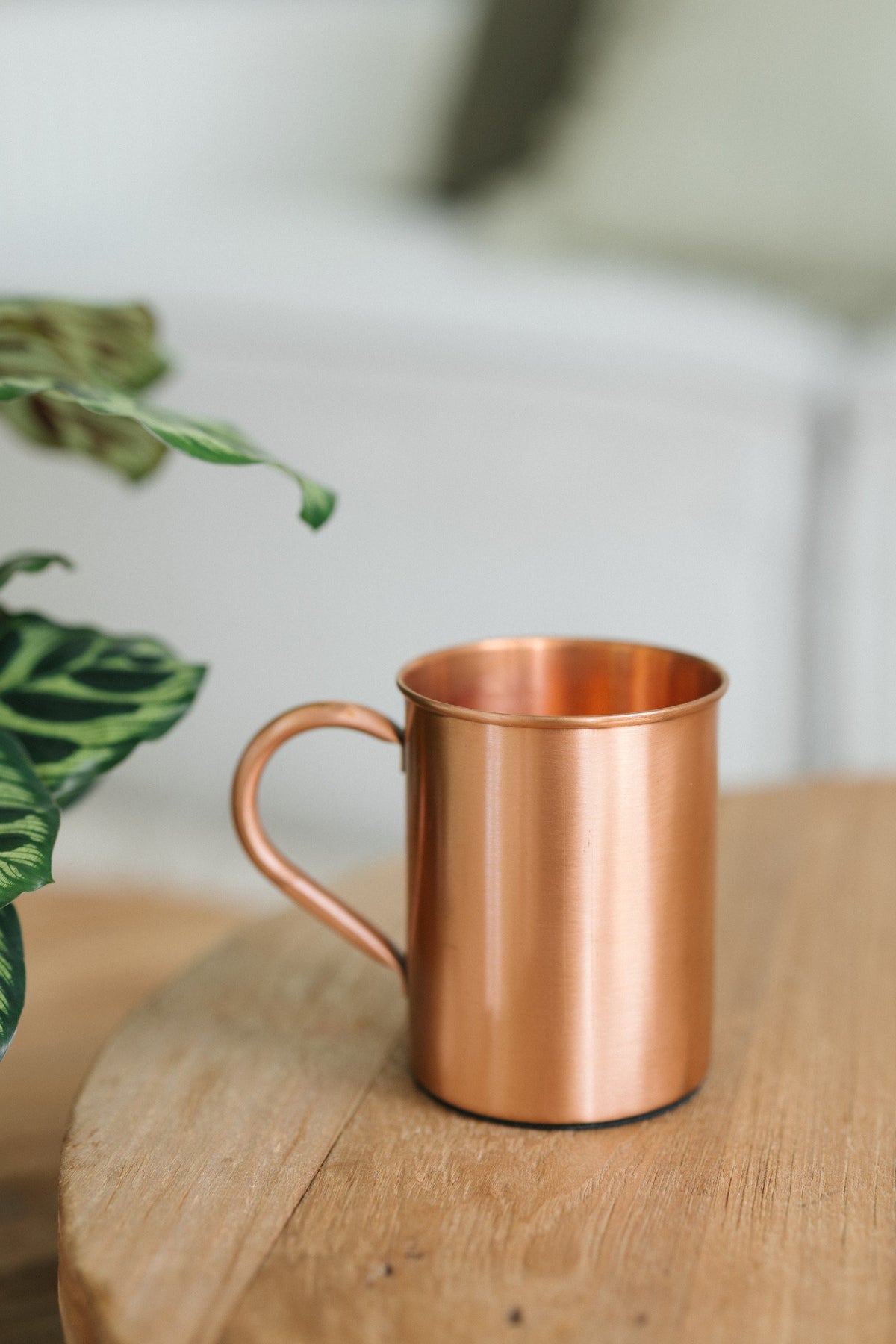 Kopero Caneca de cobre Liso, sobre uma mesa redonda de madeira em frente a um sofá