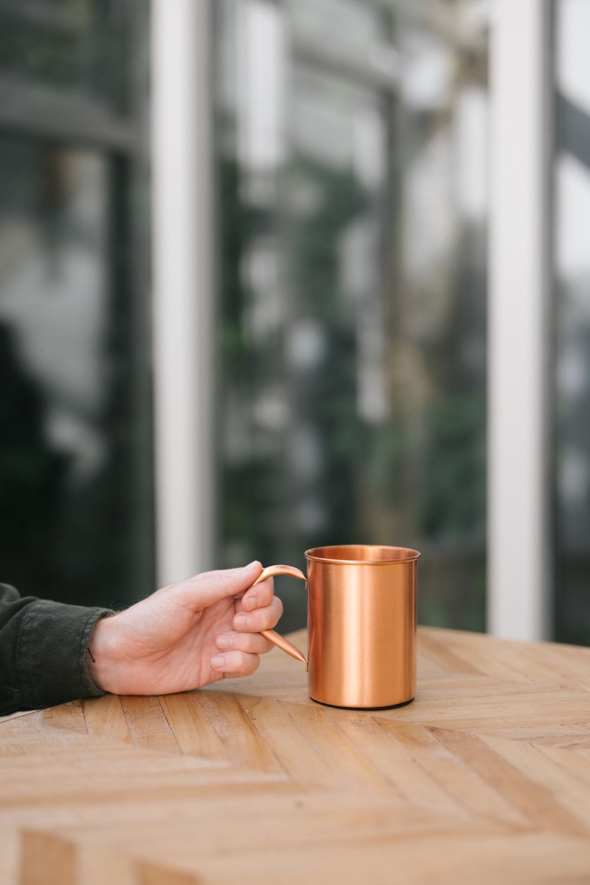 Kopero Caneca de cobre Liso, numa mesa de madeira, com uma mão na pega