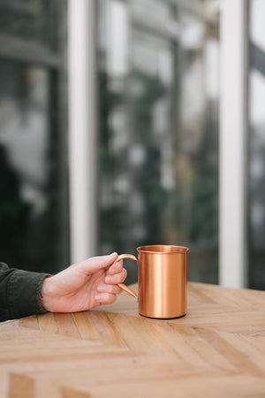 Kopero Caneca de cobre Liso, numa mesa de madeira, com uma mão na pega