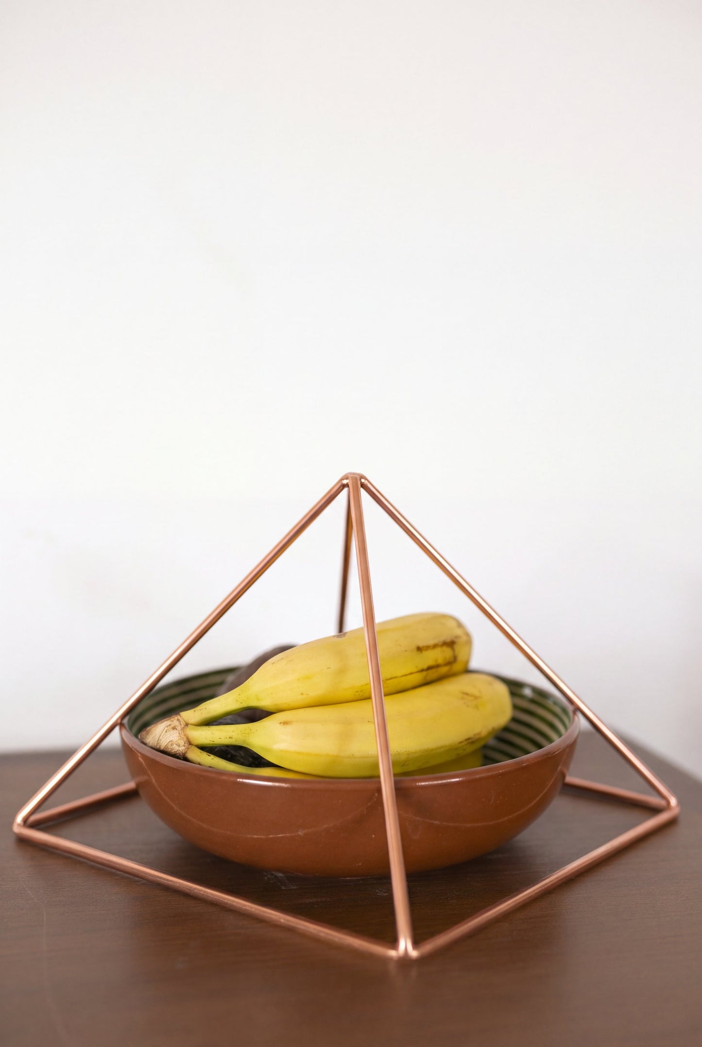Kopero Pirâmide Energizadora de Cobre Liso Grande (23,56 cm) sobre uma taça de fruta