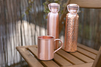 Garrafas de água de cobre Kopero Lisa e Martelada com uma caneca de cobre a condizer sobre uma mesa de jardim